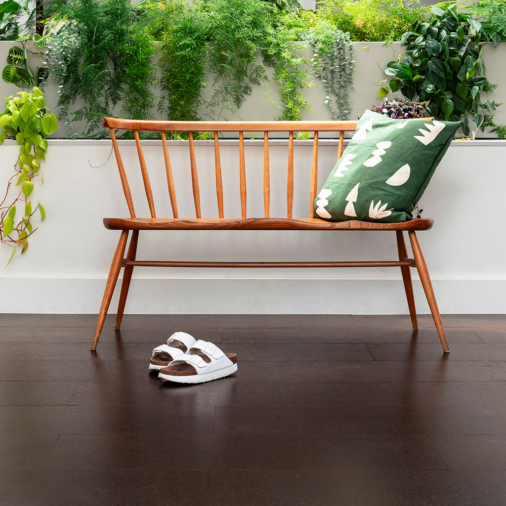 A dark brown cork floor set against a bank of hanging greenery and a wooden chair. The cork planks are made of thick 100% cork 
